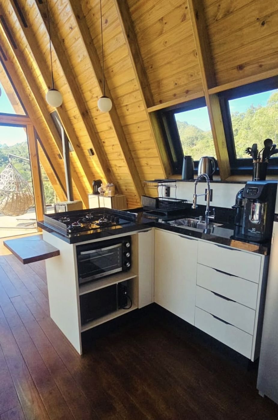 Cozinha com cooktop, forno e janelas para a mata